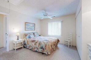 A bedroom with a bed, a nightstand, a chair, a ceiling fan, a window with blinds, and a painting on the wall. - Shoreline Stepper w/ Balcony, Free WiFi, Central AC & Washer/Dryer (Ocean City)