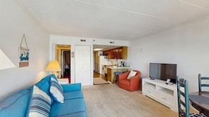 A living room with a blue sofa, a red armchair, a TV, and a kitchen in the background. - Old Town Ocean City condo with WiFi, washer/dryer, & pool - near boardwalk (Ocean City)