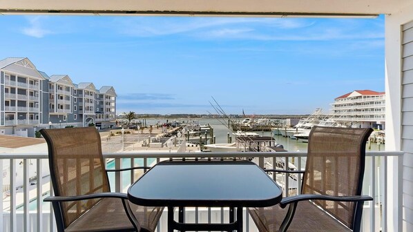Ein Balkon mit zwei Stühlen und einem Tisch, mit Blick auf einen Yachthafen mit Booten und Gebäuden.