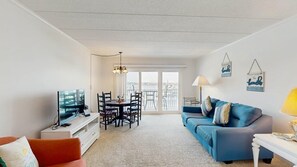 Ein Wohnzimmer mit Fernseher, Esstisch mit Stühlen, einer Couch und einem Balkon mit Blick.