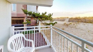A balcony with a white chair, a small tree, and a view of a sandy beach. - Partial Ocean View Condo in Oceanfront Building with Balcony, WiFi & Laundry (Ocean City)