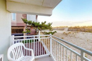 Ein Balkon mit einem weißen Stuhl, einem kleinen Baum und Blick auf einen Sandstrand.