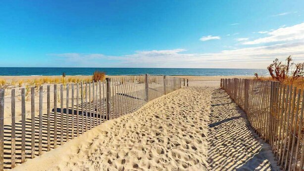 A sandy beach path with a wooden fence leading to the ocean. - Partial Ocean View Condo in Oceanfront Building with Balcony, WiFi & Laundry (Ocean City)