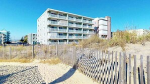 A multi-story hotel with balconies, a sandy beach in the foreground, and a clear blue sky. - Partial Ocean View Condo in Oceanfront Building with Balcony, WiFi & Laundry (Ocean City)