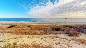 Una spiaggia con una recinzione di legno, dune sabbiose e una nave all'orizzonte.