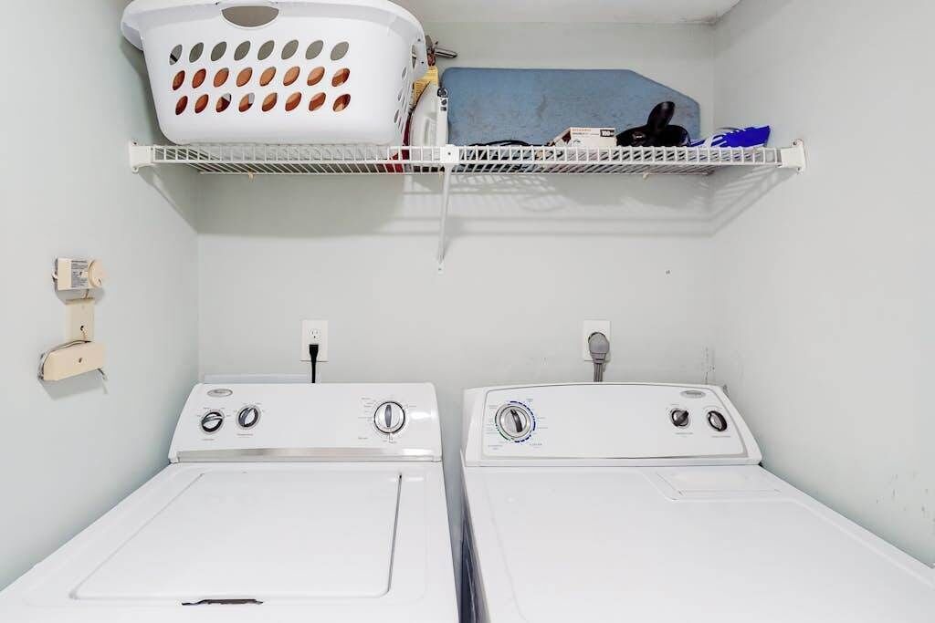 A laundry room with two washing machines, a drying rack, and a shelf with various items.