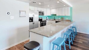 A modern kitchen with white cabinets, a granite island, and blue bar stools. - Condo One Block from the Beach w/ Balcony, AC, Laundry & Shared Pool (Ocean City)
