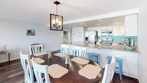 A modern kitchen with white cabinets, a central island, and a dining area with a round table and chairs. - Condo One Block from the Beach w/ Balcony, AC, Laundry & Shared Pool (Ocean City)