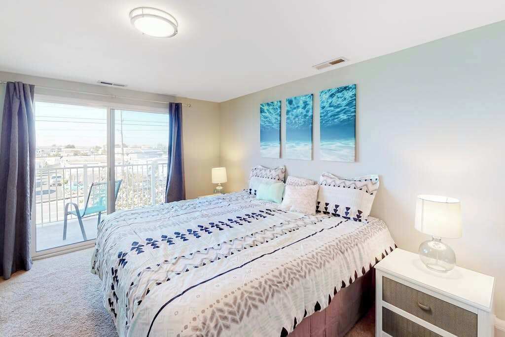 Ein Schlafzimmer mit Bett, Nachttisch, Fenster mit Vorhängen und Blick ins Freie.