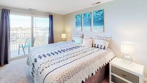 A bedroom with a bed, a nightstand, a window with curtains, and a view of the outside. - Condo One Block from the Beach w/ Balcony, AC, Laundry & Shared Pool (Ocean City)