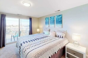 Ein Schlafzimmer mit Bett, Nachttisch, Fenster mit Vorhängen und Blick ins Freie.