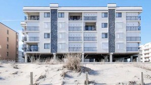 Un edificio a più piani con balconi, un tetto piano e terreno sabbioso davanti.