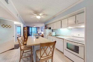 A modern kitchen with white cabinets, a dining table with chairs, a ceiling fan, and a view to the outside. - Oceanfront Condo w/ Balcony, Great Views, NEW HVAC, W/D - Walk to Northside Park (Ocean City)