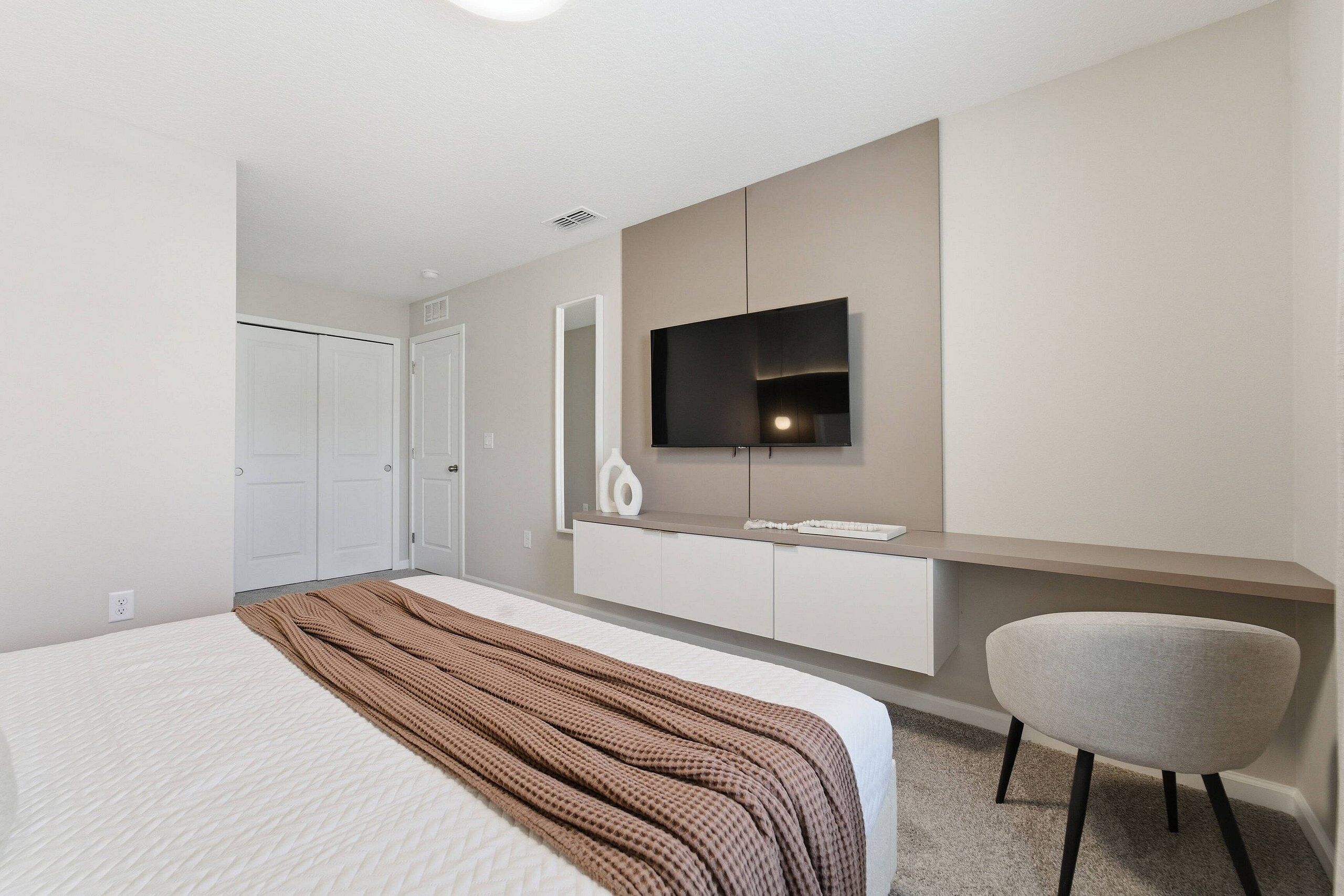 Une chambre à coucher moderne avec un lit, un téléviseur fixé au mur, un bureau et une chaise.