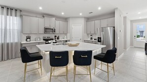 A modern kitchen with a central island, stainless steel appliances, and bar stools. - Themed 7BR Pool Home Solara, FlowRider Resort (Kissimmee)