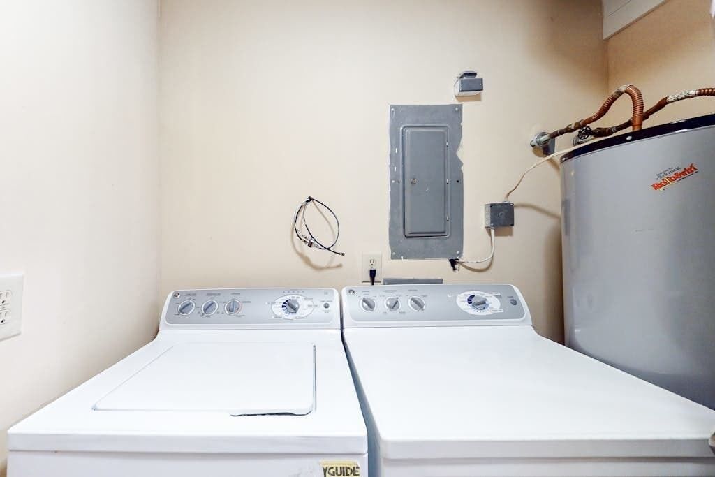 Une buanderie équipée de deux machines à laver blanches, d’un grand chauffe-eau et d’un panneau de commande.