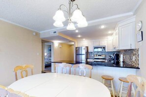 Een moderne keuken met witte kasten, een centraal eiland en een eetgedeelte met een ronde tafel en barkrukken.