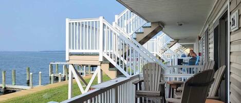 A covered outdoor area with a view of the water, a wooden deck, and a table with chairs.