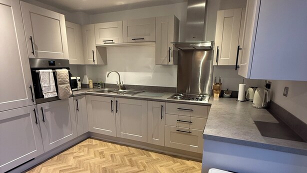 A modern kitchen with a herringbone wood floor, stainless steel appliances, and white cabinetry. - New Home w/2+ car parking and charging spaces (Knutsford)