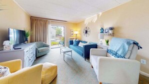 A living room with a television, sofa, armchair, and a small table. - Ocean block condo in Ocean City with balcony & steps to the beach (Ocean City)