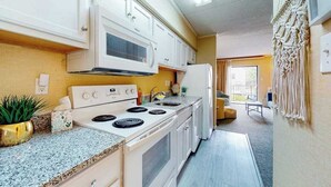 A compact kitchen with white cabinets, a microwave, stove, and a sink. - Ocean block condo in Ocean City with balcony & steps to the beach (Ocean City)