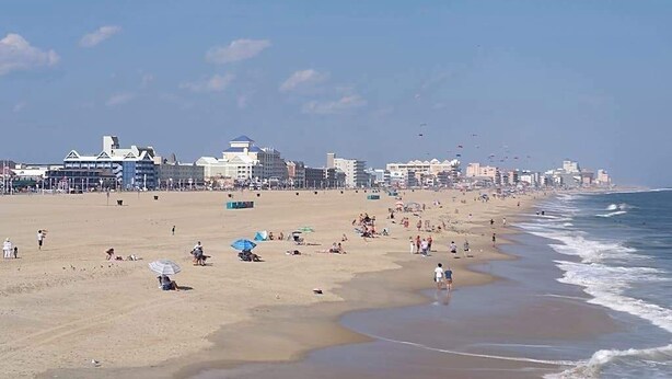 A beach with people, umbrellas, and buildings in the background. - Ocean block condo in Ocean City with balcony & steps to the beach (Ocean City)