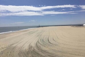 Ein breiter Sandstrand mit Spurren und einem klaren Himmel.