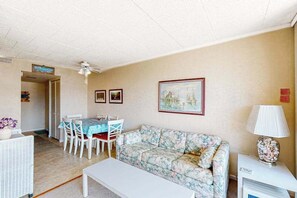 Ein Wohnzimmer mit einer Couch, einem Esstisch mit Stühlen, einem Deckenventilator und gerahmten Bildern an der Wand.