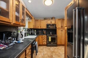 A kitchen with wooden cabinets, a black countertop, a stainless steel refrigerator, a microwave, and an oven.