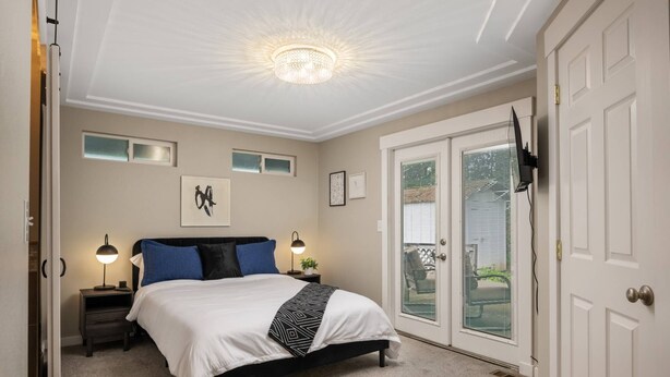 Ein Schlafzimmer mit einem Bett, zwei Nachttischen, einer Chandelüster, einer Tür mit Ausblick und einem kleinen Fenster.