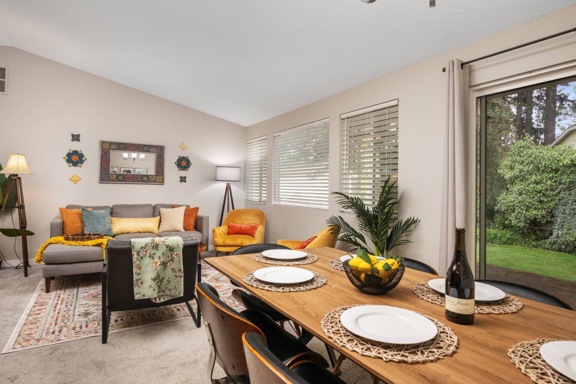 A dining area with a wooden table set for four, a sofa, a chair, and a small plant.