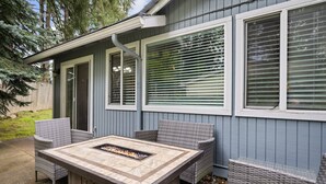 Eine Terrasse mit Feuerstelle, Korbmöbeln und einer überdachten Sitzgruppe, sowie ein Haus mit blauen Wandpaneelen und weißen Verzierungen.