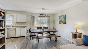 Una cocina moderna con armarios blancos, una mesa de comedor con bancos y vistas al exterior.
