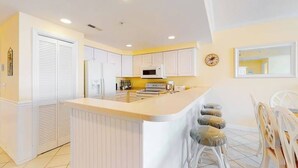 A kitchen with white cabinets, a central island, and a dining area with white chairs. - Family-Friendly Condo near the Beach w/Fireplace, W/D, Shared Outdoor Pool, A/C (Ocean City)