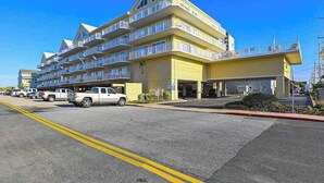 A multi-story hotel with balconies, a parking lot, and a clear blue sky. - Family-Friendly Condo near the Beach w/Fireplace, W/D, Shared Outdoor Pool, A/C (Ocean City)