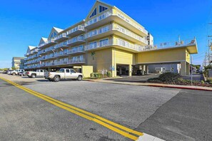 A multi-story hotel with balconies, a parking lot, and a clear blue sky. - Family-Friendly Condo near the Beach w/Fireplace, W/D, Shared Outdoor Pool, A/C (Ocean City)