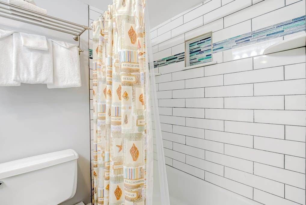 Een badkamer met witte betegelde wanden, een douchegordijn met een strandthema en een witte handdoek aan een rek.