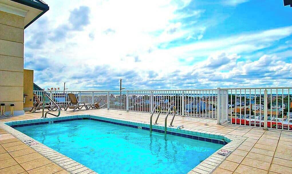 Une piscine entourée d’une clôture blanche, un ciel dégagé et une vue sur la mer.