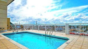 A swimming pool with a white fence, a clear sky, and a view of the sea. - Family-Friendly Beach Condo: Balcony, w/d, shared outdoor pool & gym (Ocean City)