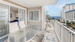 A balcony with a glass table and chairs, a view of the sea, and a building with multiple balconies. - Family-Friendly Beach Condo: Balcony, w/d, shared outdoor pool & gym (Ocean City)