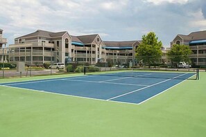 A tennis court with a green surface, surrounded by multi-story buildings with large windows and a flat roof. - Light-Filled Waterfront Condo w/ Marsh & Bay Views, Deck, Shared Pool & Tennis (Ocean City)