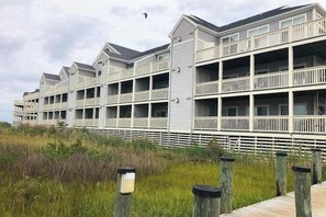 Ein Strandhotel mit mehreren Balkonen, einer Holzterrasse und einem Rasenbereich.