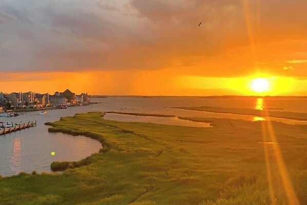 Un atardecer sobre un río, con edificios a la izquierda y zonas verdes al frente.