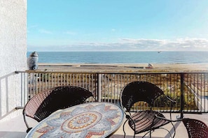 A balcony with a mosaic table and chairs, overlooking a beach with a distant boat. - Oceanfront condo with pool, AC, balcony, & washer/dryer (Ocean City)