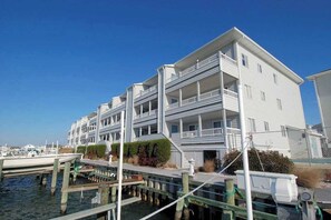 A multi-story waterfront building with balconies, a dock, and a clear blue sky. - Wonderful bayfront condo overlooking the marina with pool, balcony & fireplace (Ocean City)