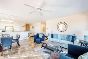 A spacious living area with a kitchen in the background, a ceiling fan, and a decorative wall piece. - Waterfront Condo on the Canal w/ Deck & Shared Pools/Tennis - Walk to the Beach (Ocean City)