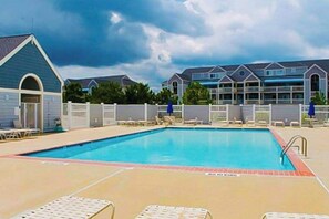 A swimming pool with lounge chairs, a fenced area, and a row of buildings in the background. - Waterfront Condo on the Canal w/ Deck & Shared Pools/Tennis - Walk to the Beach (Ocean City)