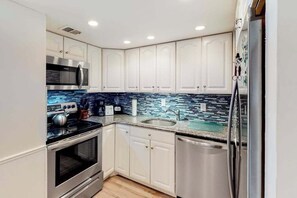 A modern kitchen with white cabinets, stainless steel appliances, and a blue-tiled backsplash. - Irene 607 (Ocean City)