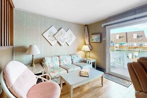 A room with a sofa, two chairs, a small table, and a view of buildings through a large window. - Gullway Getaway (Ocean City)