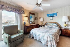 Een hotelkamer met een bed, een stoel, een dressoir, een plafondventilator en uitzicht op buiten.